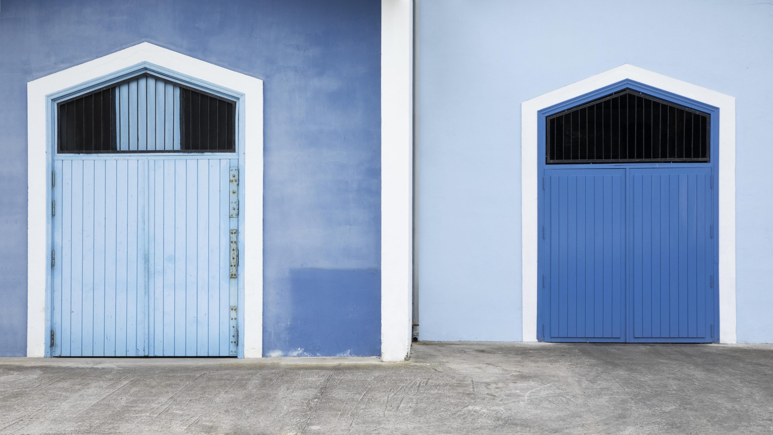 Vista frontal de duas fachadas de casas lado a lado, uma azul escura com uma porta azul clara e outra azul clara com uma porta azul escura.