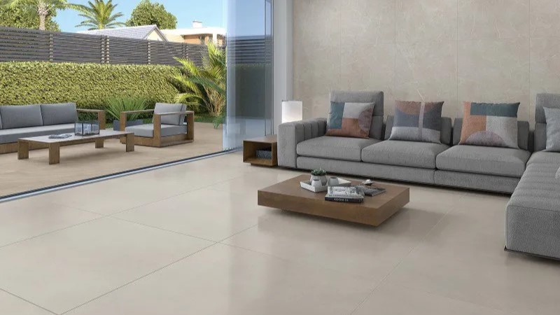 sala de estar com piso porcelanato bege claro, sofá cinza e mesa de centro de madeira com lateral de porta de vidro voltada para o jardim