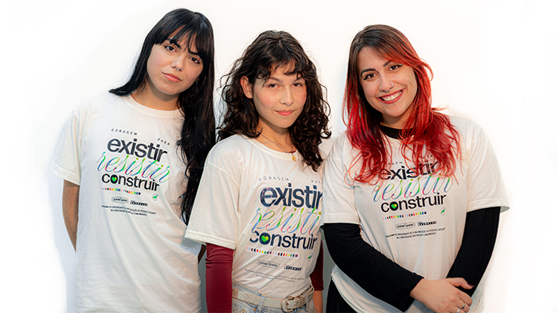 Três jovens com camisetas brancas sorrindo para a câmera