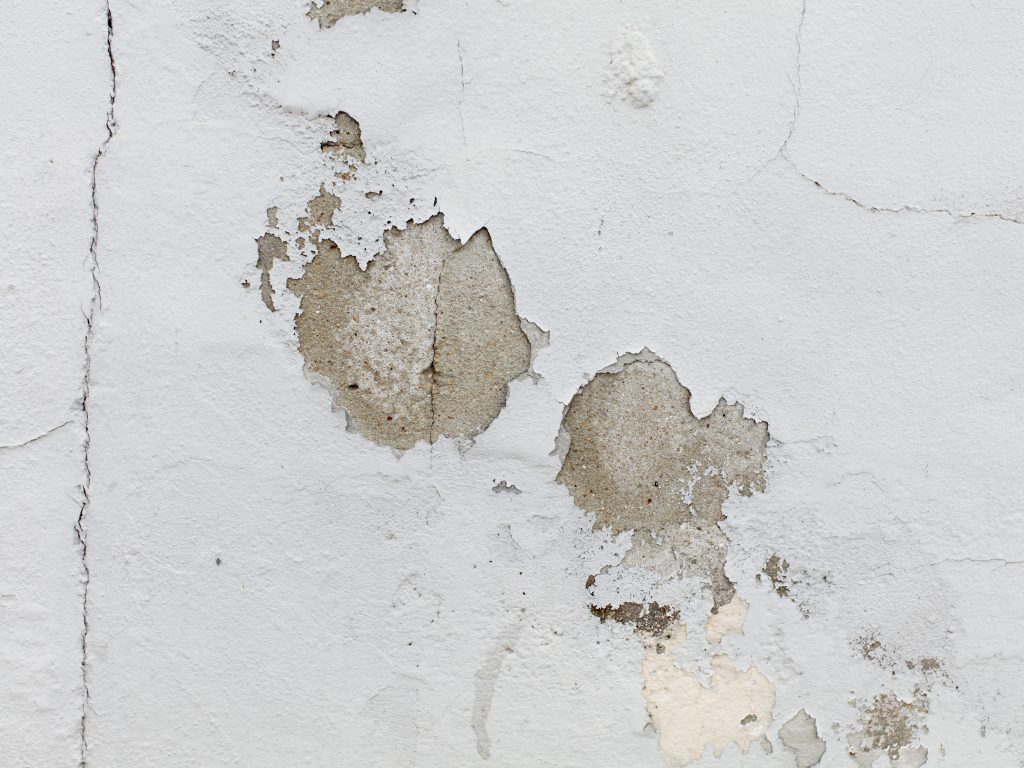 Pintura descascada em parede branca com manchas