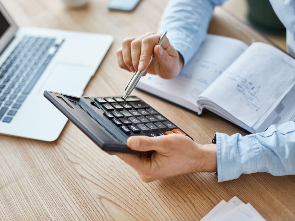 Pessoa usando calculadora e laptop em mesa.