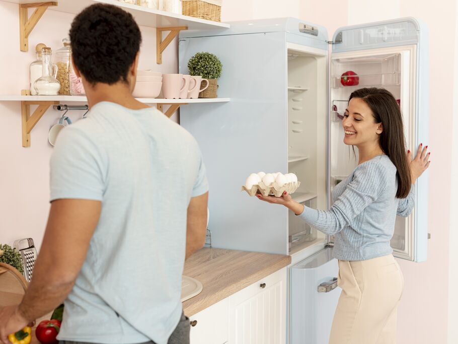Casal na cozinha organizando alimentos na geladeira