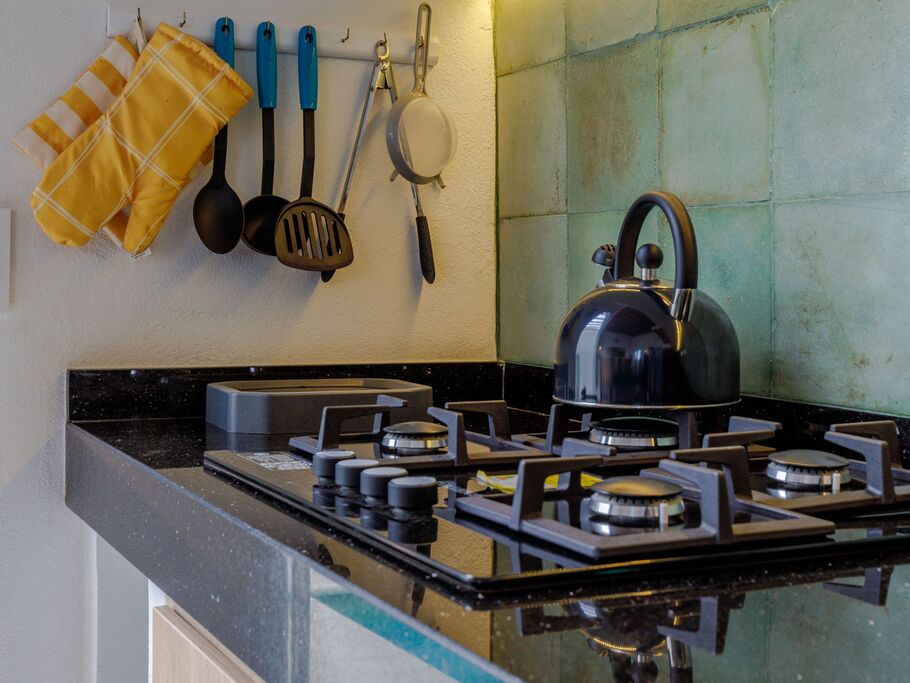 Bancada de cozinha com fogão, utensílios e chaleira.