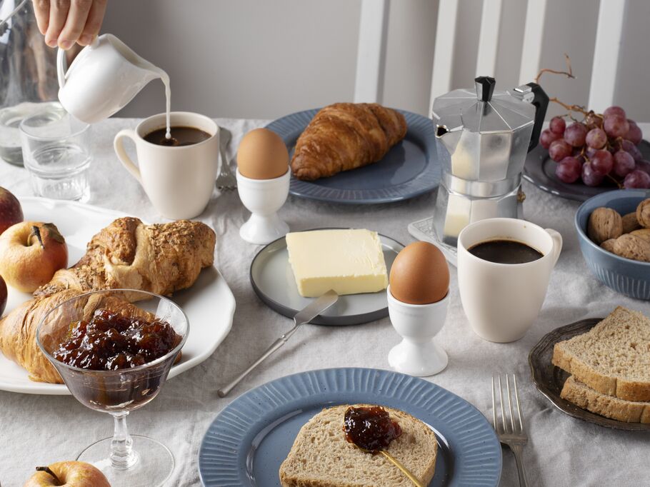 Mesa de café da manhã com pães, frutas e café.